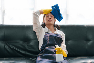 Young Asian woman tired from doing housework. Asian female housewife who is tired from cleaning the house sits with her back the sofa. - obrazy, fototapety, plakaty