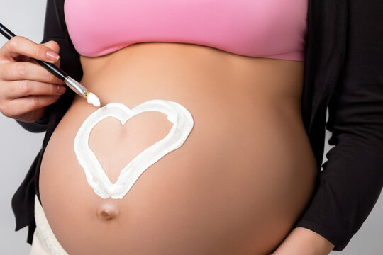 pregnant girl. a young pregnant girl draws a heart on her big belly with white paint and a small brush