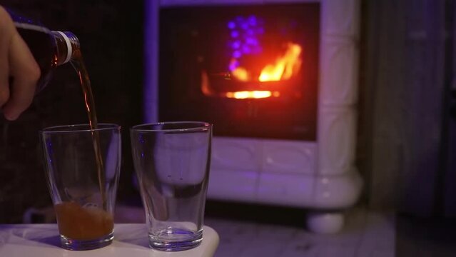 Slow motion beer pouring into two glass with fireplace and flames on background. Xmas holidays indoor.