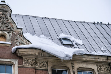 A lump of snow and ice on the edge of the roof of the house. Thaw, chalking snow danger in the city.