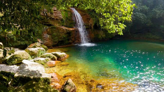 Jungle waterfall with white waters running down Rocky ridge of hill to blue green water of lagoon or pool. Sun rays passing through clear water. Rangshokham falls of Meghalaya.