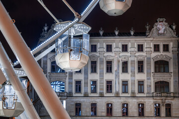 Ferris wheel in the city center. Historic urban architecture in the background. Light illumination....