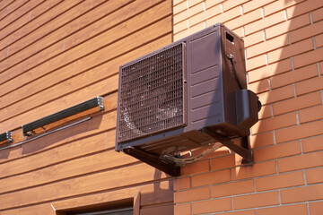 The air conditioner compressor is black on the wall of the building