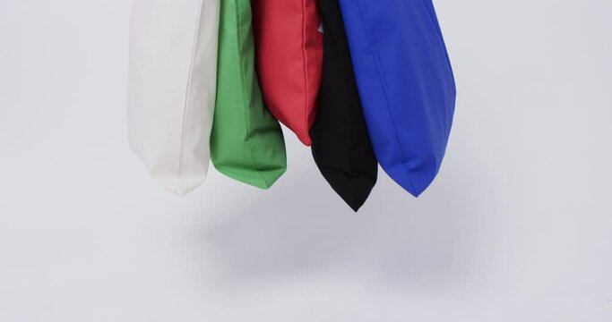 A collection of colorful tote bags in white, green, red, black, and blue hangs against a plain backg