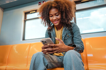 Happy young African American traveling woman passenger smile and using smart mobile phone in subway train station. Enjoying travel - obrazy, fototapety, plakaty
