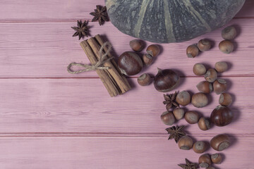 Autumn flatlay with pumpkin, chestnuts, star anise, cinnamon and cobnuts on a pink wooden...