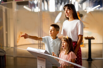 Mom with kids are excited to interact with a robot, visiting together science museum. Concept of...