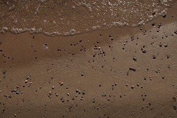 Top view of stones lying on a wet sand beach and sea water with bubbles.