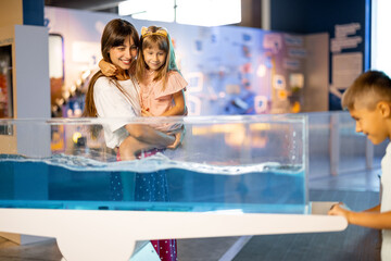 Mom with kids learn physics interactively on a model that shows physical phenomena while visiting a...