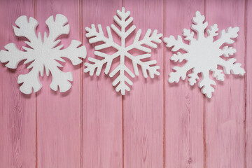 Three white snowflakes on a pink wooden background topview. New Years flatlay with copyspace