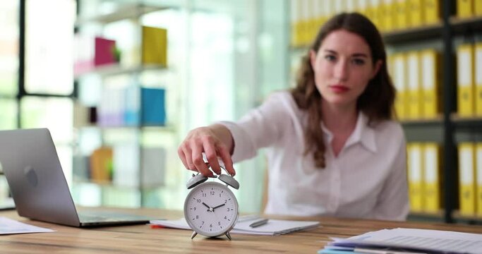 Business woman puts on alarm clock working place in office. Concept of time management and deadlines
