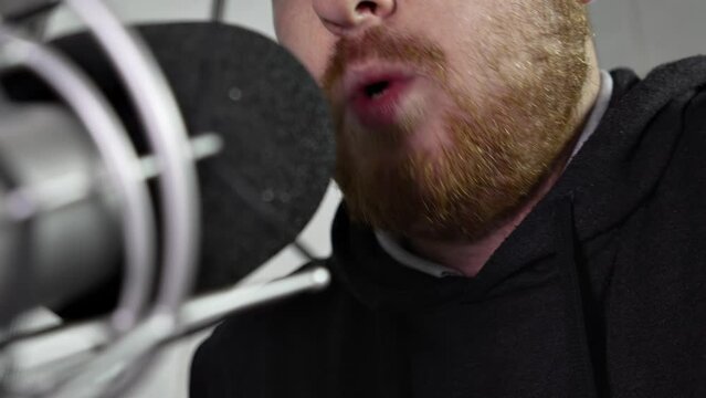 close-up of the mouth of a middle-aged man with a red beard, who conducts a radio broadcast in front of a professional microphone, tells useful information for listeners. a young man records a podcast