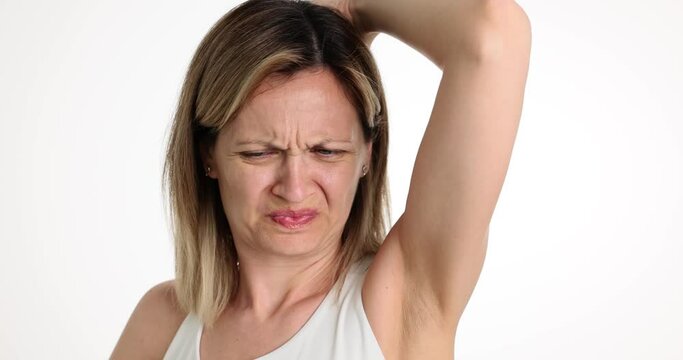 Worried woman with unhappy face checks smell of armpit. Bad underarm odor and bad smelling deodorant