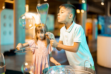 Little girl and boy make soap bubbles, while playing together and having fun in a science museum....