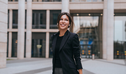 Obraz premium Cheerful businesswoman with a confident smile standing outside an office building, representing success and professional positivity