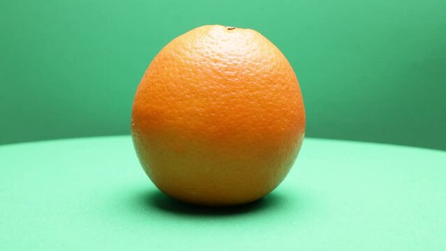 Whole ripe orange fruit hand held shake rotate green background