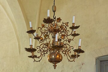 Metal chandelier with candles hanging from roof of a church.