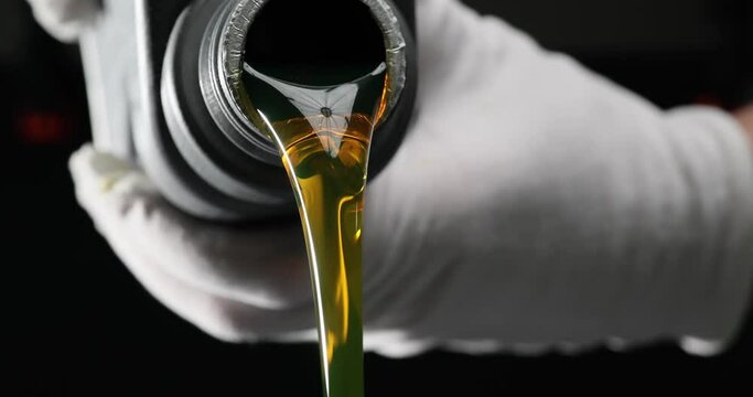 Worker in a white glove pours oil on black background. Slow filling of engine oil from a bottle