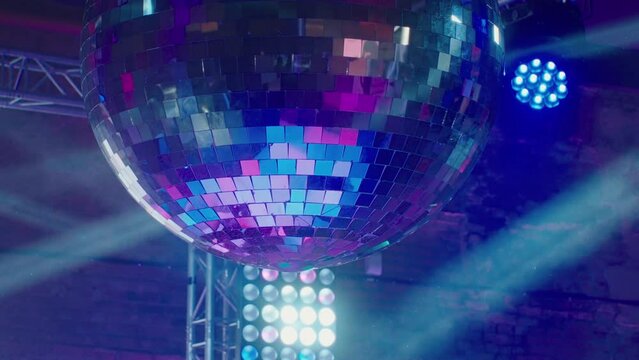 A huge disco ball is spinning against the background of the stage with lighting devices illuminating it with rays of light. A beautiful glass ball at a renault dance party at the club. Colorful.