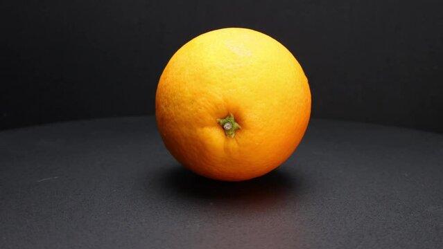 Whole ripe orange fruit hand held shake rotate black background