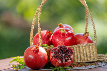 Pomegranate in wooden basket on wooden table in garden, Pomegranate with slices on blurred greenery background.