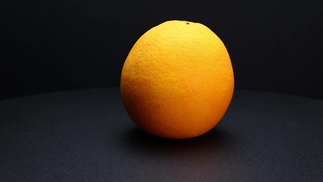 Whole ripe orange fruit hand held shake rotate black background