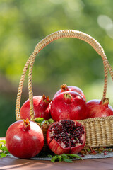 Pomegranate in wooden basket on wooden table in garden, Pomegranate with slices on blurred greenery background.