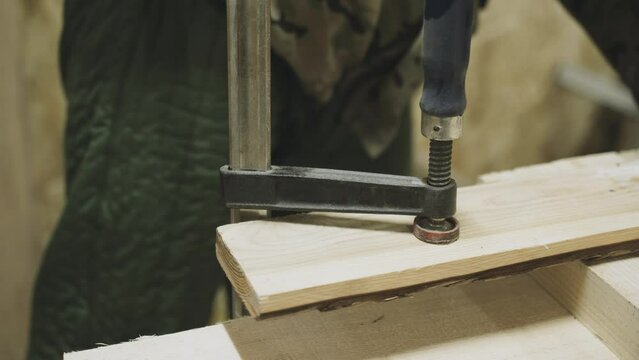 A carpenter secures a piece of wood using a screw clamp. Fastening the part. Close-up.