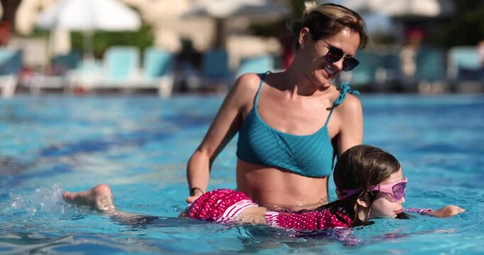 Happy mother with daughter swimming in pool in summer. Vacation free time and learning to swim