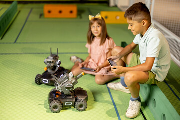 Kids playing with robotic cars controlling them with remote controls on a playground in science museum. Concept of children's entertainment and new technologies