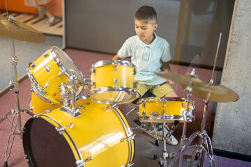 Fototapeta premium Little boy playing on a real drums, having fun while visiting a science museum