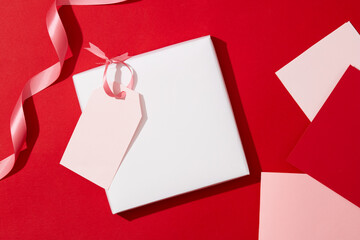 The paper cards are decorated with pink ribbons on a red background. Space for advertising. Love theme with good wishes. Copy space, top view.