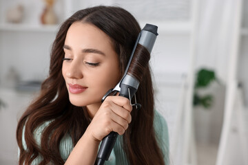 Beautiful woman using curling hair iron indoors. Space for text