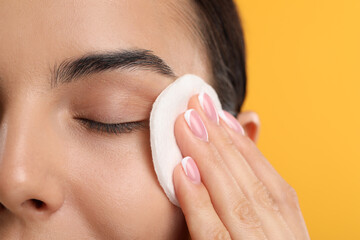 Beautiful woman removing makeup with cotton pad on orange background, closeup. Space for text