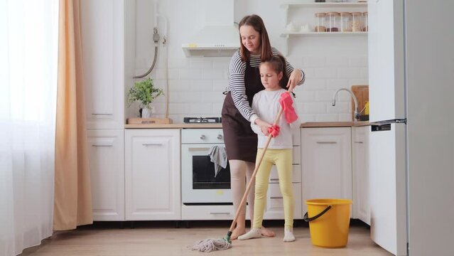Caucasian mother and cute little daughter doing wet cleaning kitchen floor two female generations family together doing household chores mom teaching her child to clean the house
