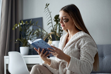 Woman at home reading a book, wearing black eye patches. Cosmetology and skin care