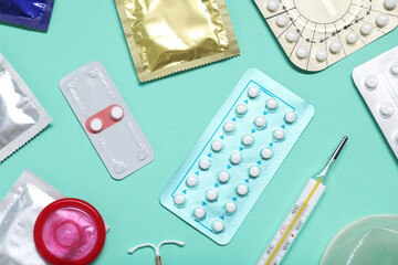 Contraceptive pills, condoms, intrauterine device and thermometer on turquoise background, flat...