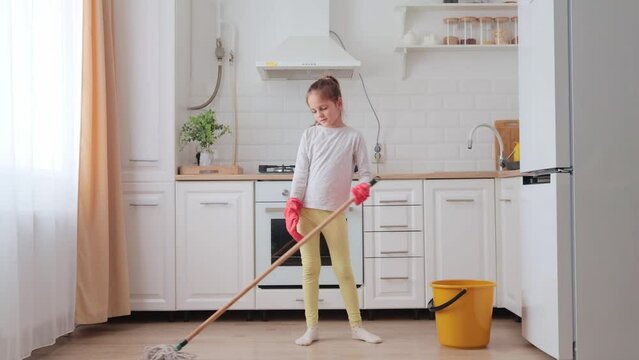 Little tired exhausted little girl in rubber gloves washing kitchen floor with mop expressing sadness feeling fatigue helping her mother doing household chores