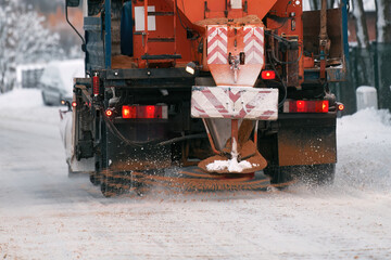 Orange truck removes snow. Snow plow on highway salting road. Tractor performing street deicing.