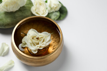 Tibetan singing bowl with water and beautiful rose flowers on white background, space for text