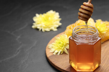 Pouring sweet honey from dipper into jar at grey table, space for text