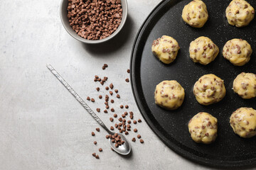Tray with raw chocolate chip cookie balls and spoon on gray table, flat lay