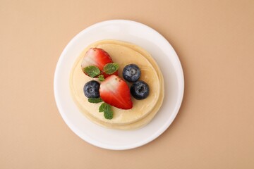 Stack of tasty pancakes with fresh berries and mint on beige background, top view