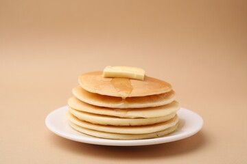Delicious pancakes with butter and honey on beige background