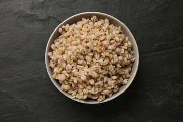 Tasty pearl barley porridge in bowl on dark textured table, top view