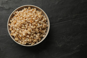 Tasty pearl barley porridge in bowl on dark textured table, top view. Space for text