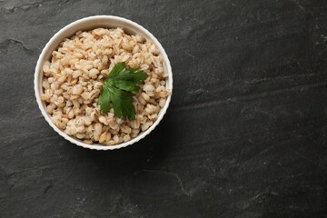 Tasty pearl barley porridge in bowl on dark textured table, top view. Space for text