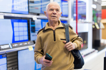 Elderly man choosing TV in showroom of electronics store