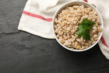 Tasty pearl barley porridge in bowl on dark textured table, top view. Space for text