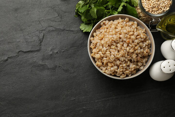 Tasty pearl barley porridge in bowl on dark textured table, flat lay. Space for text